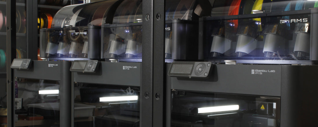 Vista de impresoras 3D BambuLab P1S y sistema AMS en un entorno de taller, mostrando filamentos de colores y varios objetos impresos, destacando la avanzada tecnología de impresión 3D disponible en Jutlo Studio.