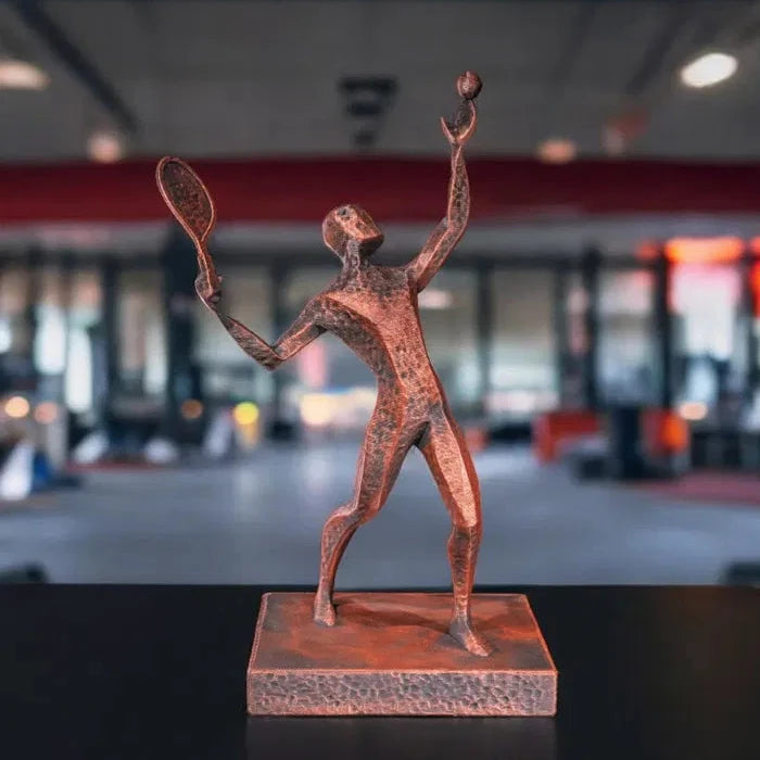 Escultura de un jugador de tenis realizando un saque, vista frontal, mostrando la precisión y elegancia del movimiento en un diseño estilizado de bronce envejecido.